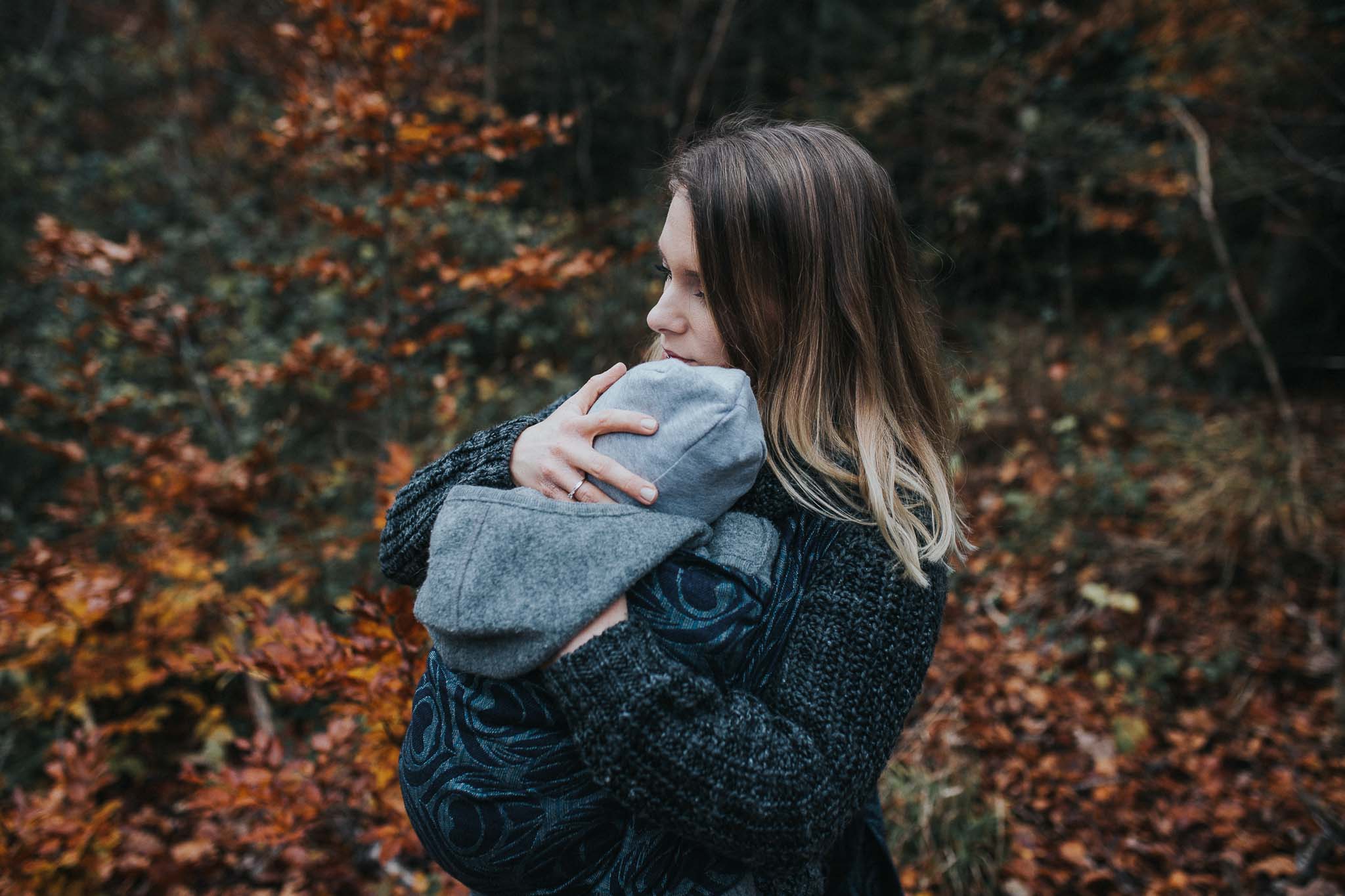 Eine Mutter trägt ihr Kind in einem Tragetuch und hält es liebevoll fest