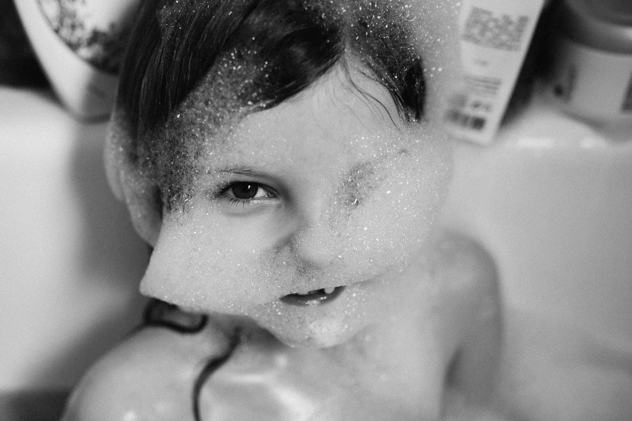 kleines Mädchen mit Schaum im Gesicht in der Badewanne